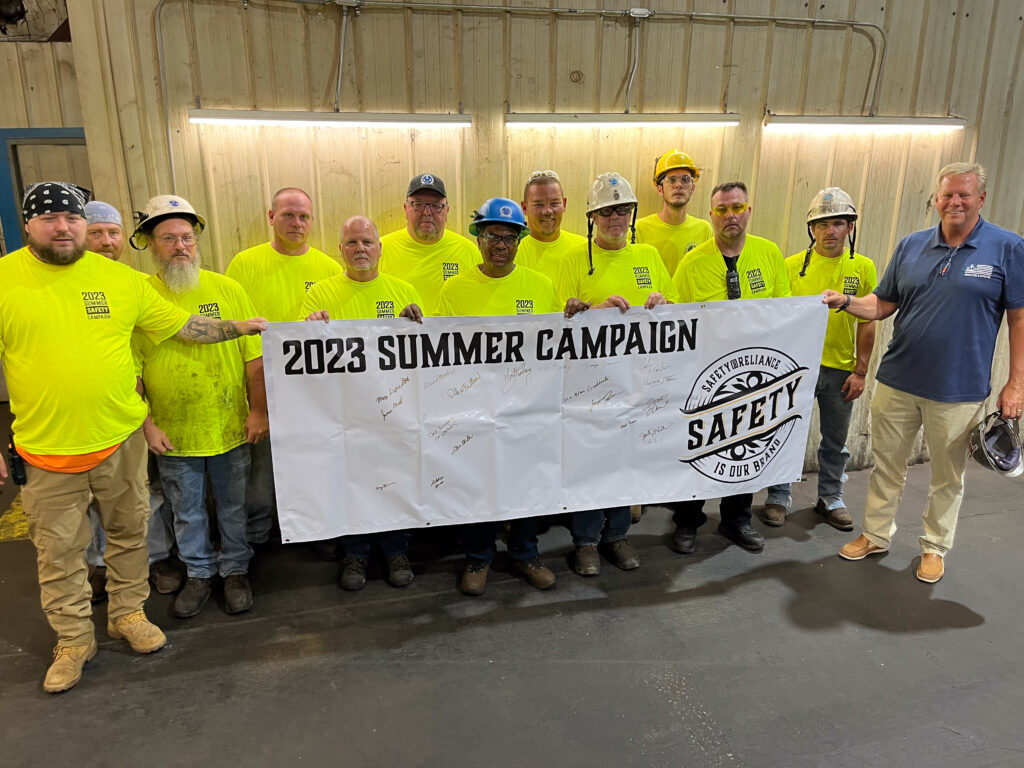 Group of Steel Workers displaying a Safety banner.
