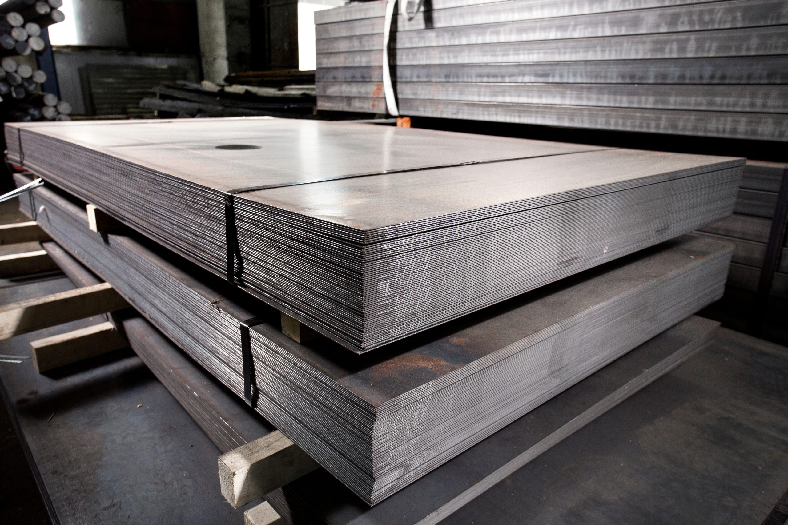 A stack of carbon steel sheet banded together sitting on a wooden palette in an industrial warehouse