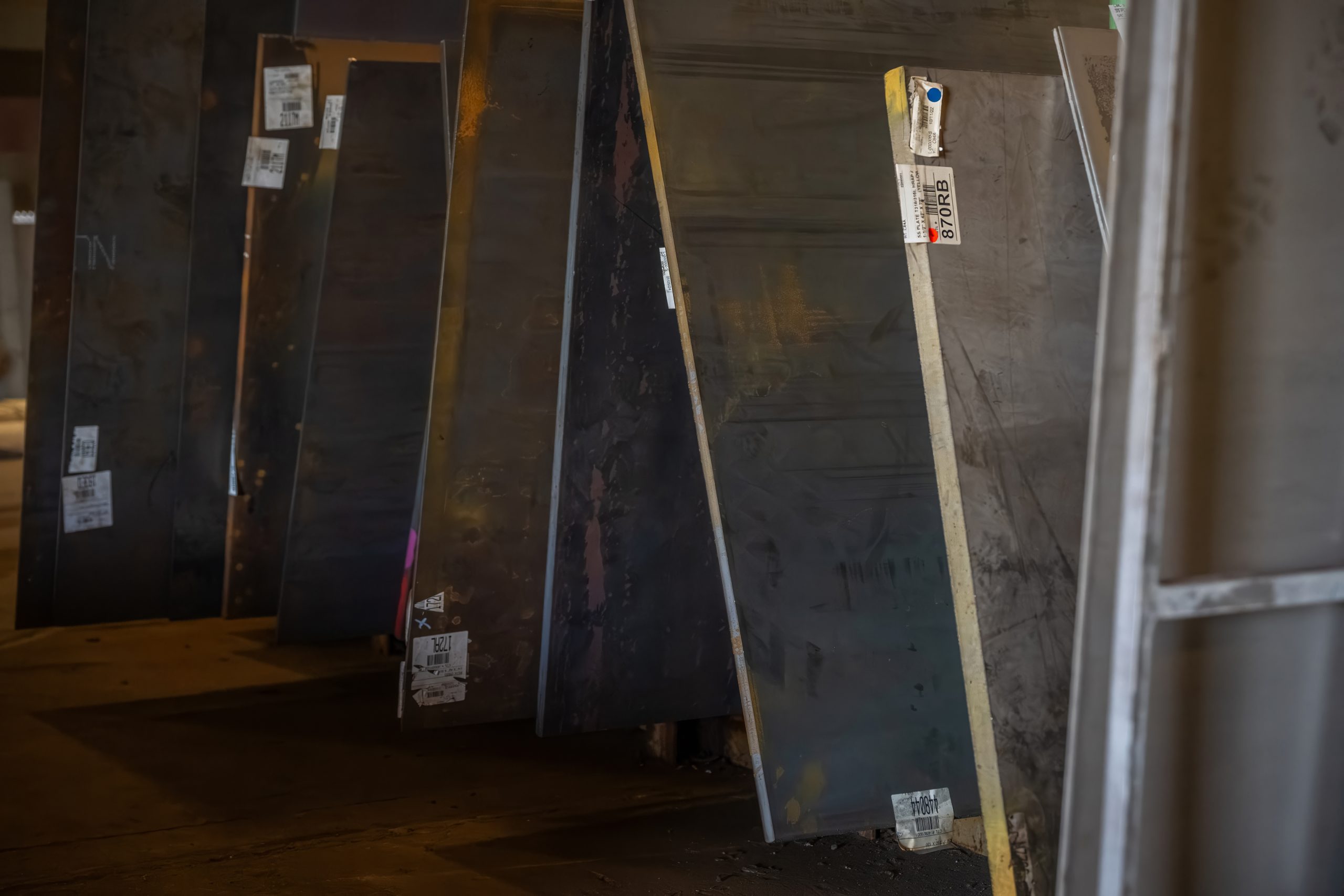 Carbon steel plates stacked vertically on wooden pallets inside a warehouse