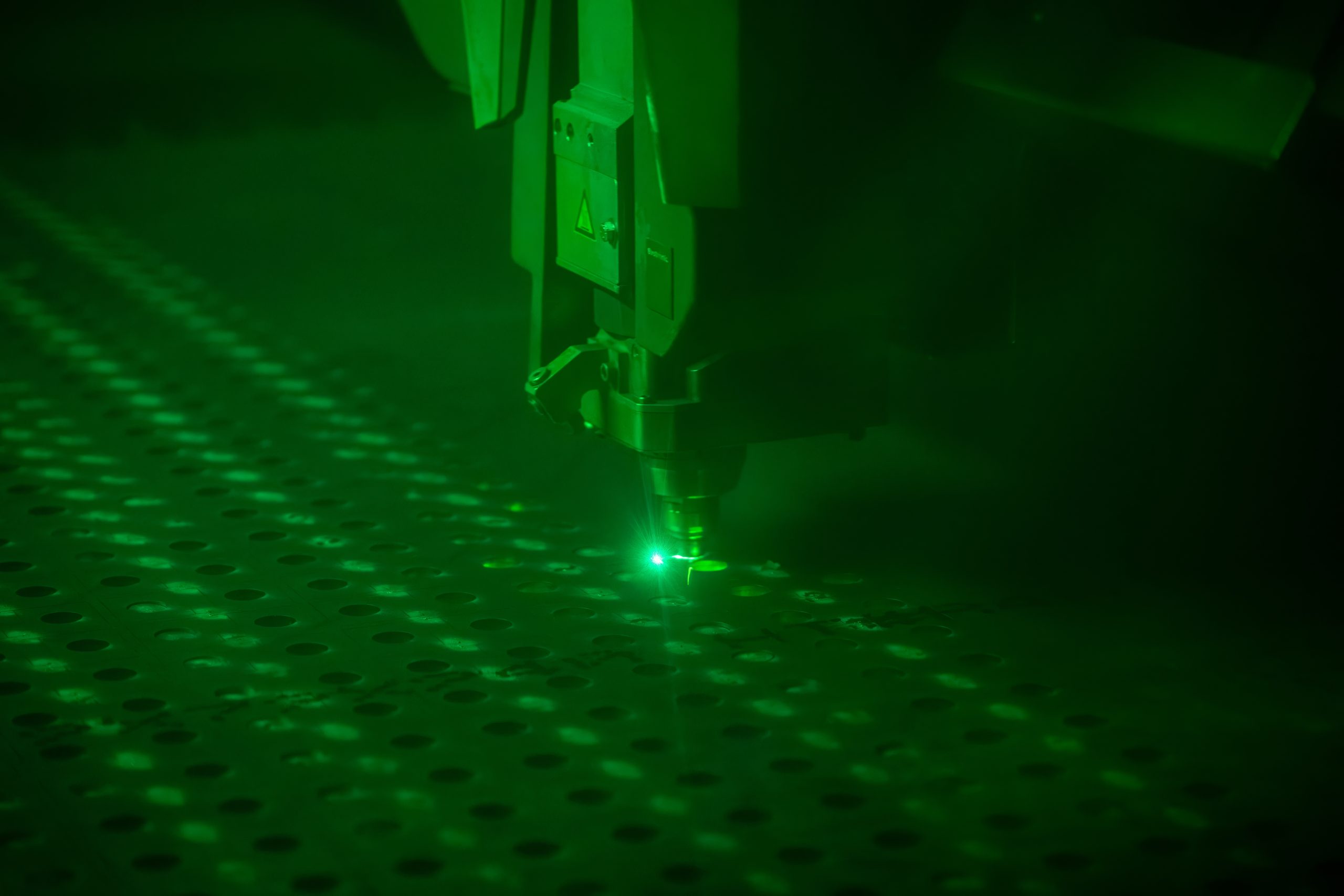 Close up of a laser cutting through a steel plate with green colored sparks.