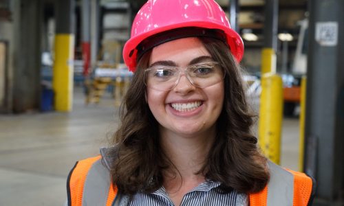 Careers Page Young career woman wearing pink hard hat, orange vest, and safety glasses inside of a warehouse. Her pale skin is offset by her green eyes and long brown curly hair. Siskin Steel Careers allow you to choose the perfect path for you.