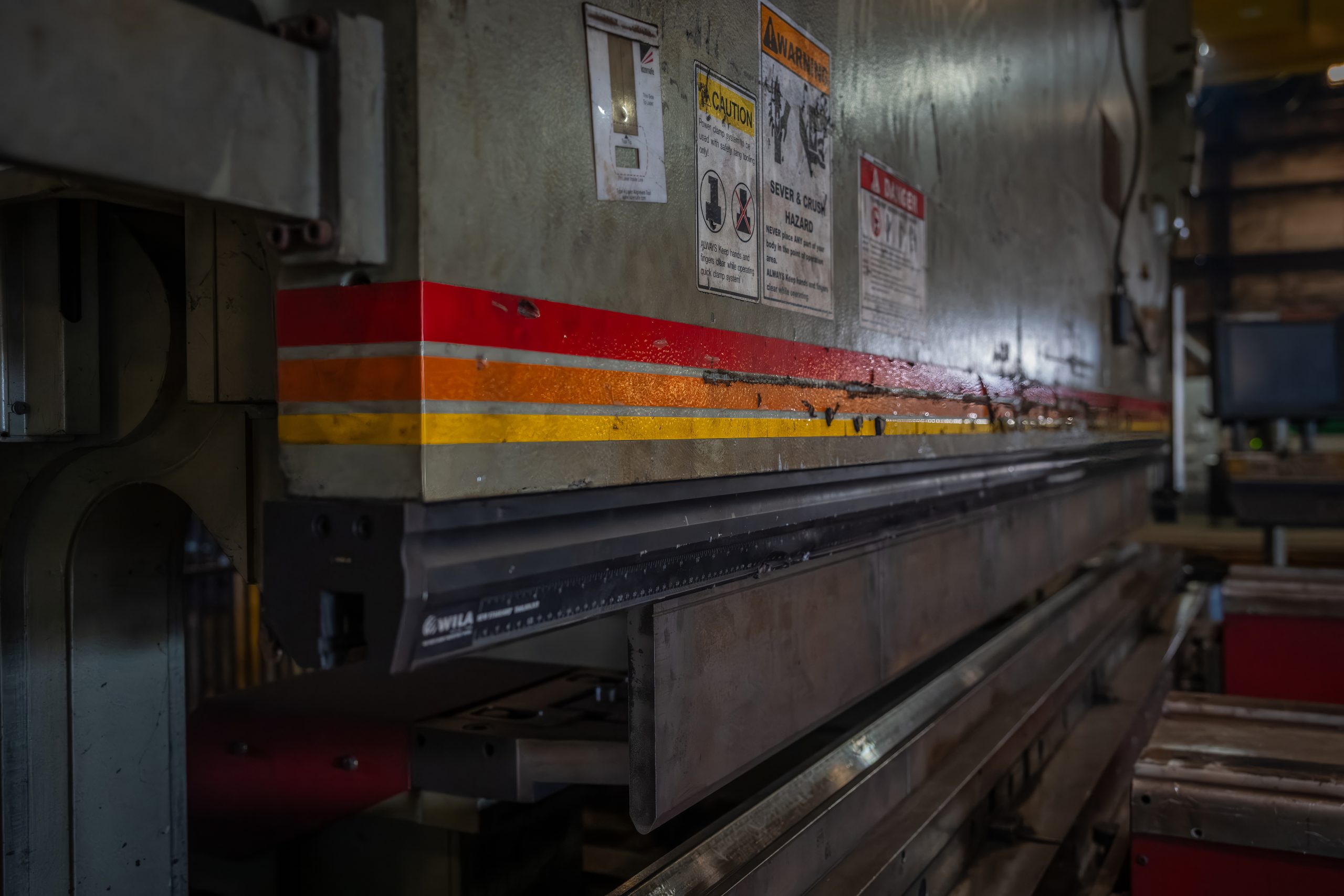 Metal forming machine from the side. The clamps in the center are the primary focus with three different colored stripes above the clamps and safety stickers.