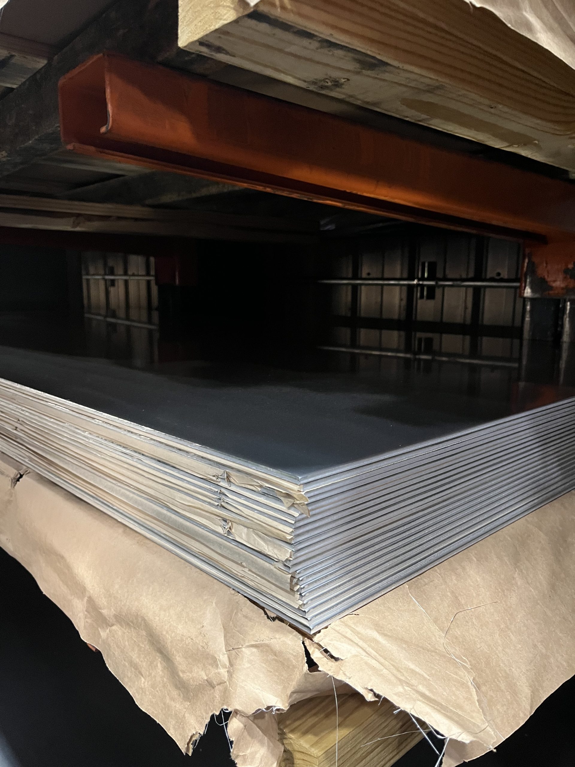 Aluminum sheet stack sitting on a wooden palette in a tower for metal storage with brown paper separating each sheet