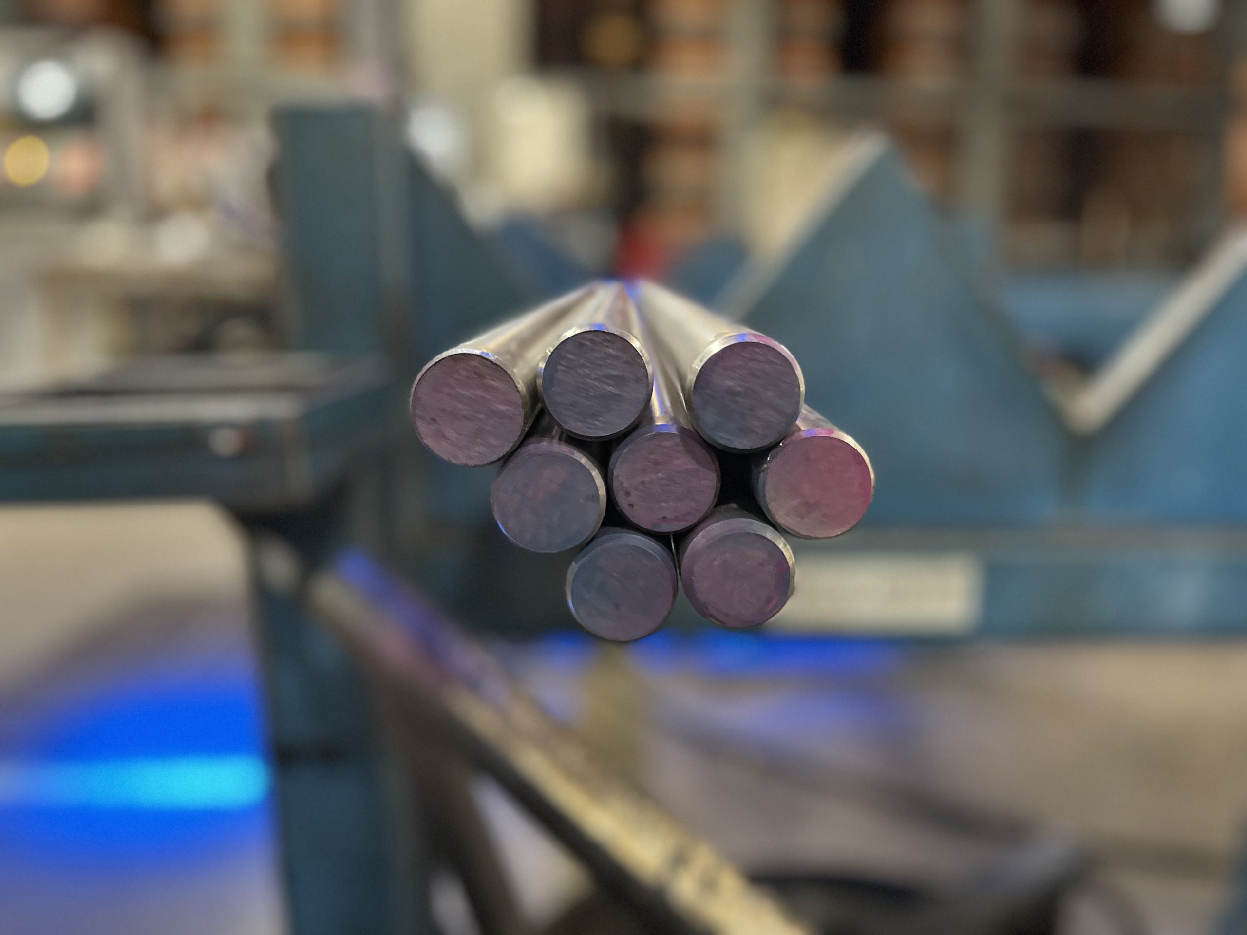 Stacked stainless steel round bars with a shiny finish laying on a blue conveyor