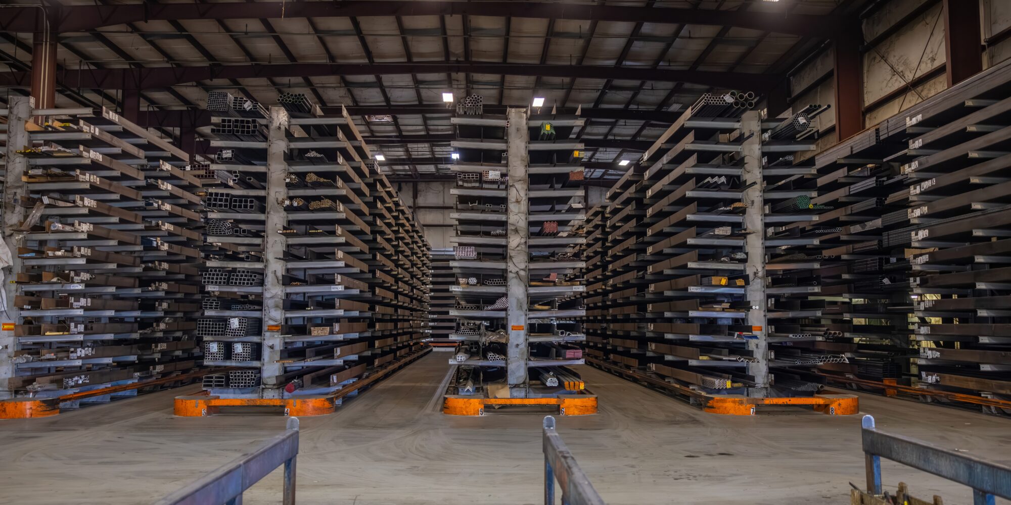 Four rows of steel stock stored on high shelves in an organized warehouse.